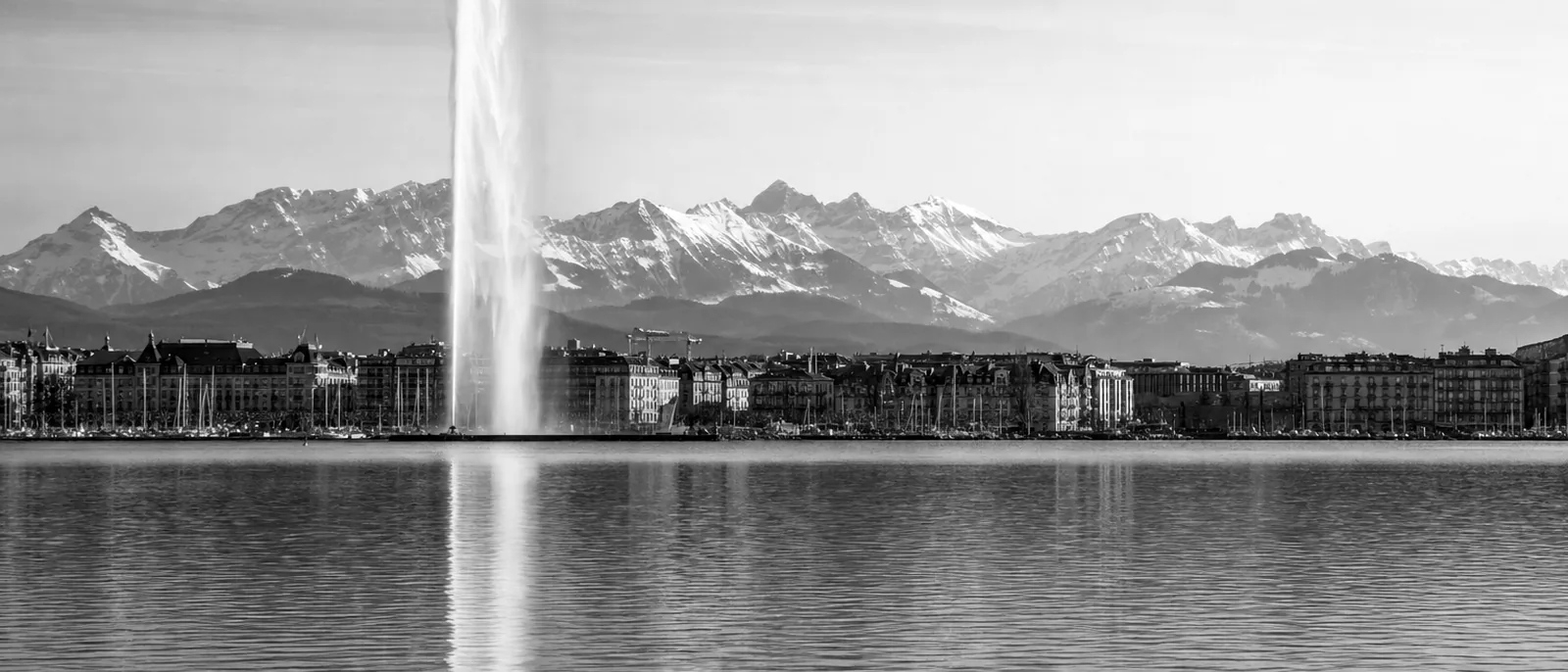 Le lac Léman, la rade de Genève et les Alpes enneigées avec le Jet d'Eau, évoquant Genève terrain neutre du dialogue sur l'IA